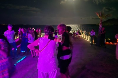 Des personnes dansent en plein air sous un éclairage coloré, avec une vue nocturne sur la mer en arrière-plan.