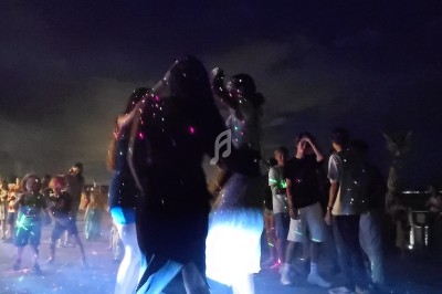 Des personnes dansent en plein air sous des lumières colorées, entourées d'autres participants en soirée nocturne.