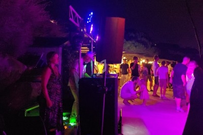 Personnes dansant et discutant lors d'une soirée en plein air, éclairée par des lumières colorées.