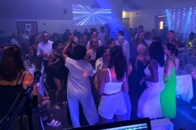 Des personnes dansent et s'amusent dans une salle éclairée par des lumières colorées, avec un DJ en arrière-plan.