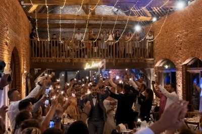 Salle de réception en fête avec des invités levant leurs bras sous des guirlandes lumineuses dans une ambiance chaleureuse.