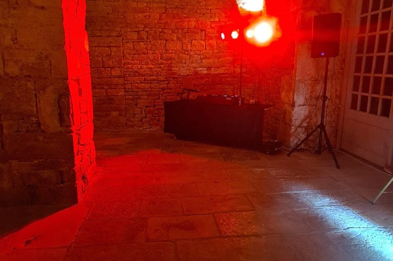 Salle voûtée en brique avec éclairage rouge ambiant - platine DJ et équipement sonore visibles.