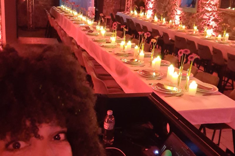 Salle voûtée en pierre avec deux tables dressées, bougies allumées, éclairage rose - vue depuis la console de DJ.