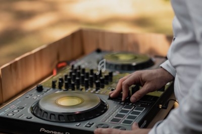 Une personne utilise une table de mixage DJ en extérieur, entourée d'un décor naturel flou.