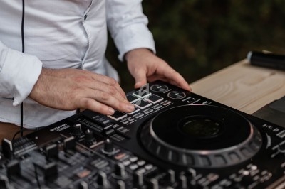 Un DJ en chemise blanche utilise une table de mixage en extérieur.