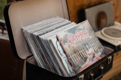 Valise ouverte contenant des disques vinyles, posée sur un support en extérieur devant des étagères en bois.