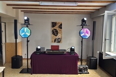 Installation de matériel de sonorisation et d'éclairage dans une salle avec une table recouverte d'une nappe violette.