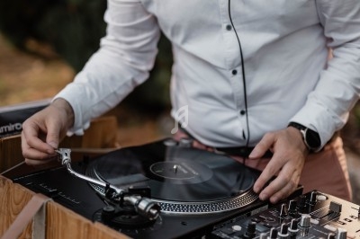 Un DJ en chemise blanche manipule un vinyle sur une platine, avec une table de mixage à ses côtés.