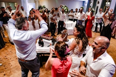 Des invités applaudissent autour d'une mariée et d'un gâteau lors d'une fête dans une salle décorée.