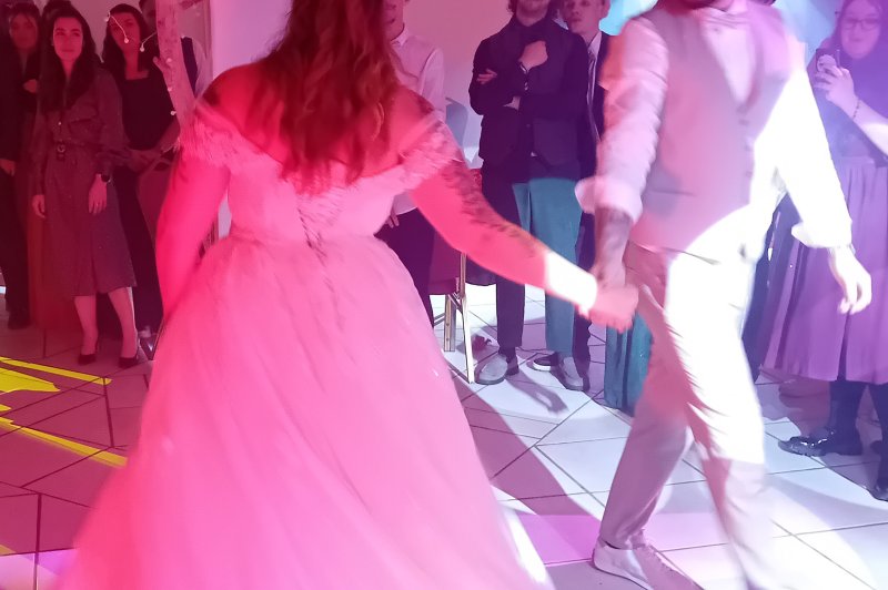 Salle intérieure éclairée en rose vif avec convives dansant sur piste, draperies blanches et ambiance festive.